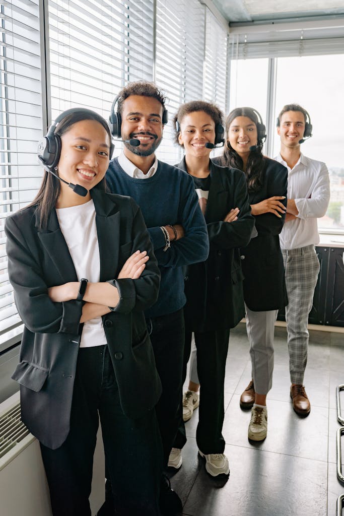 Diverse group of call center professionals wearing headsets, standing confidently in an office.